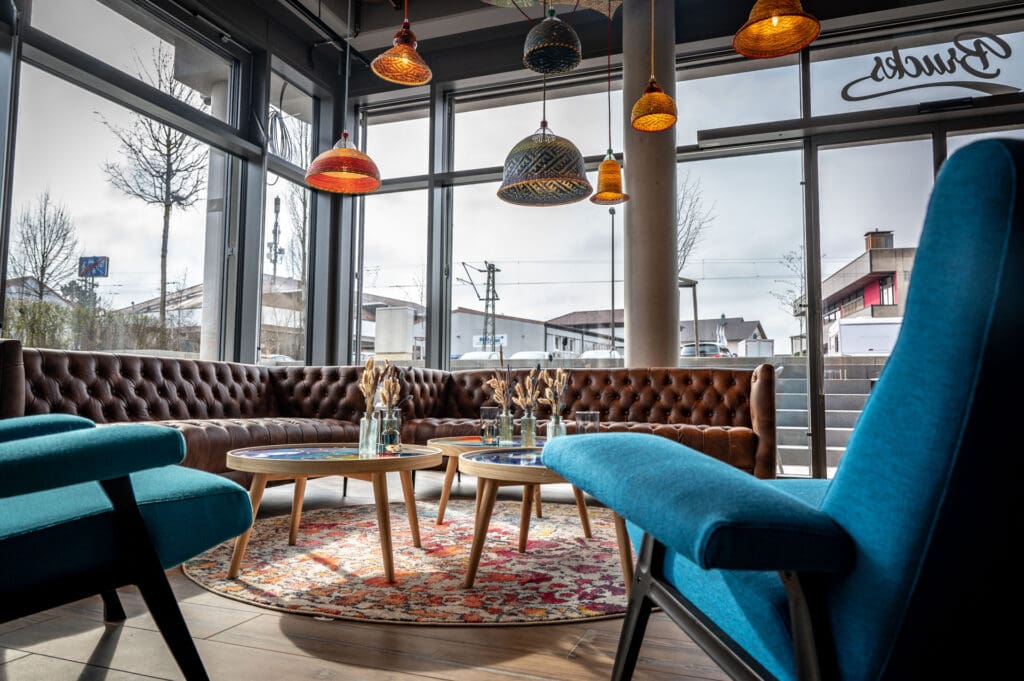 Gemütliche Sitzecke im Brucks Café und Restaurant im Brucklyn Quartier mit braunen Lederbänken, blauen Sesseln, runden Holztischen und dekorativen Hängelampen